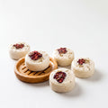a collection of small, round, white treats with red and green toppings, arranged on a wooden tray and a white surface.